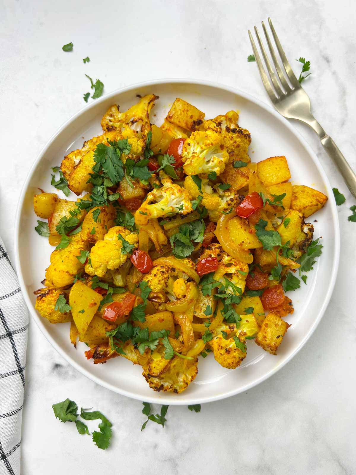 air fryer aloo gobi served on a plate garnished with cilantro and fork on the side