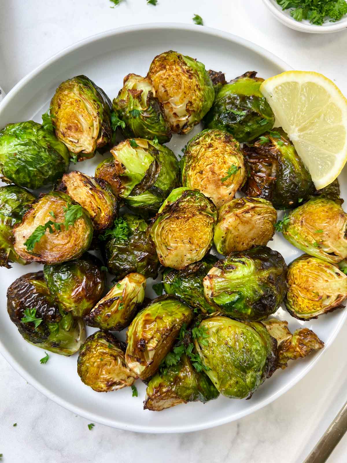 roasted brussels sprouts served in a plate with lemon wedge on the side and garnished with parsley