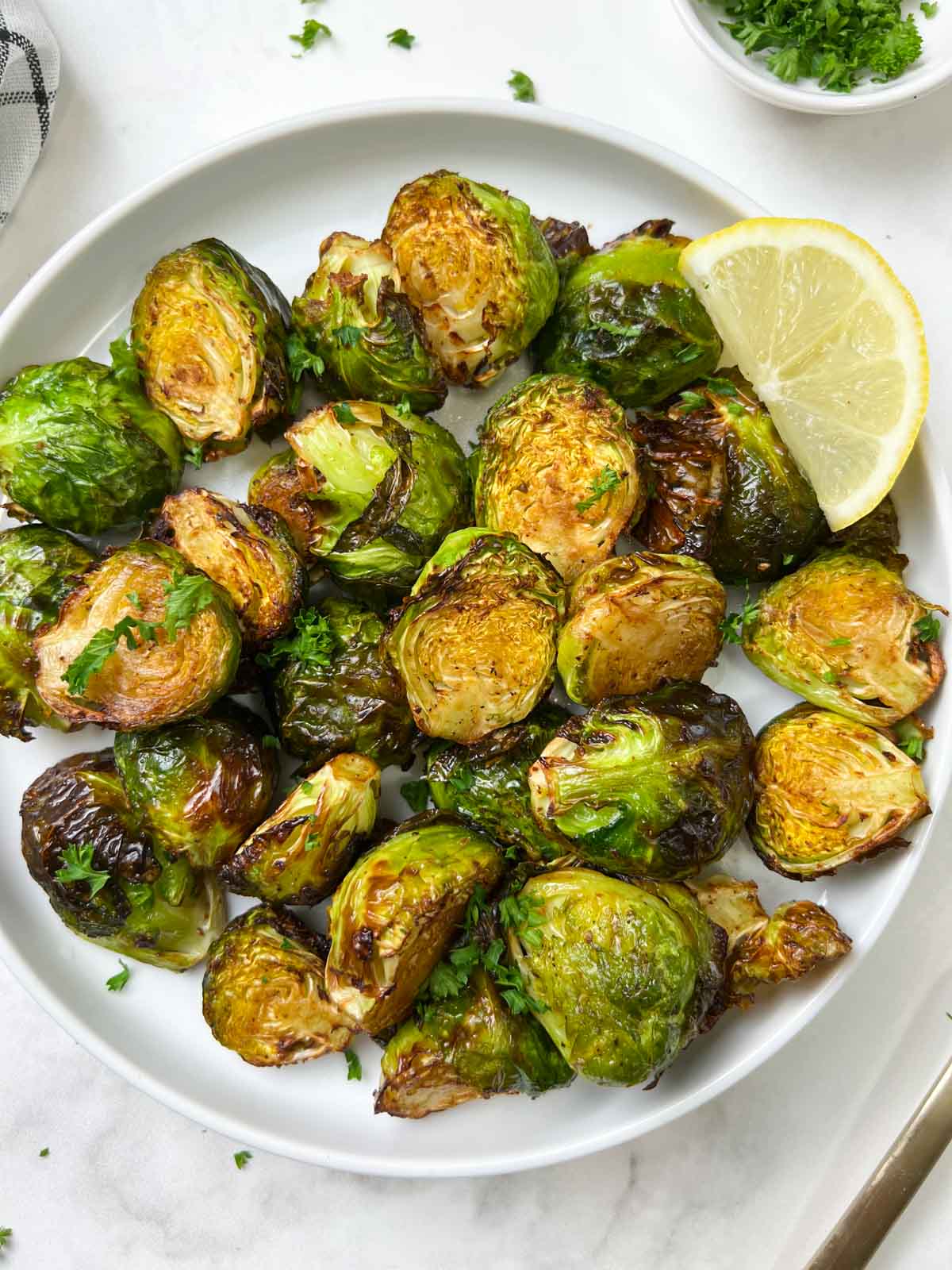 roasted brussels sprouts served in a plate with lemon wedge on the side and garnished with parsley