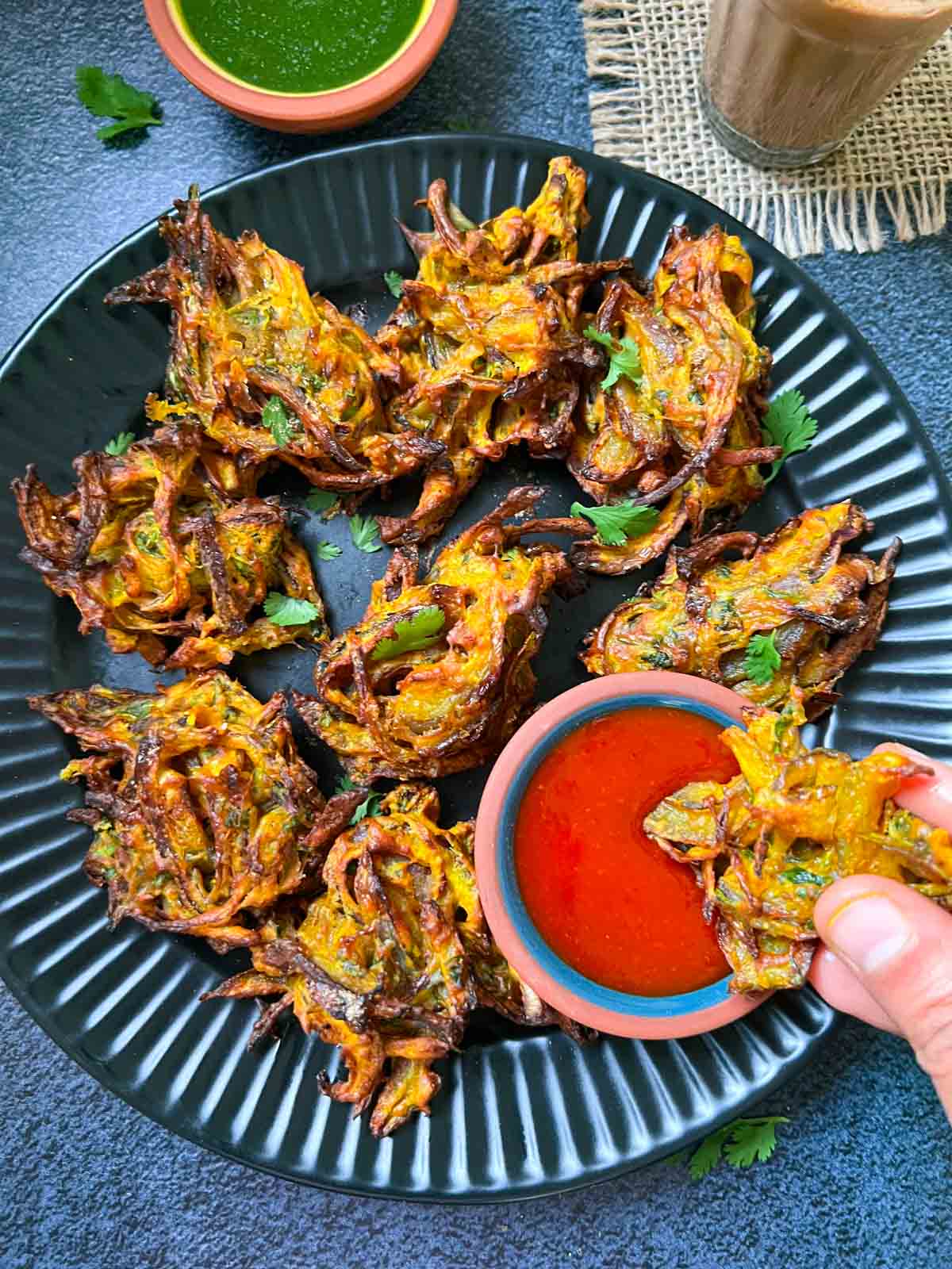 air fryer onion pakoda served on a plate with ketchup and green chutney on the side with tea