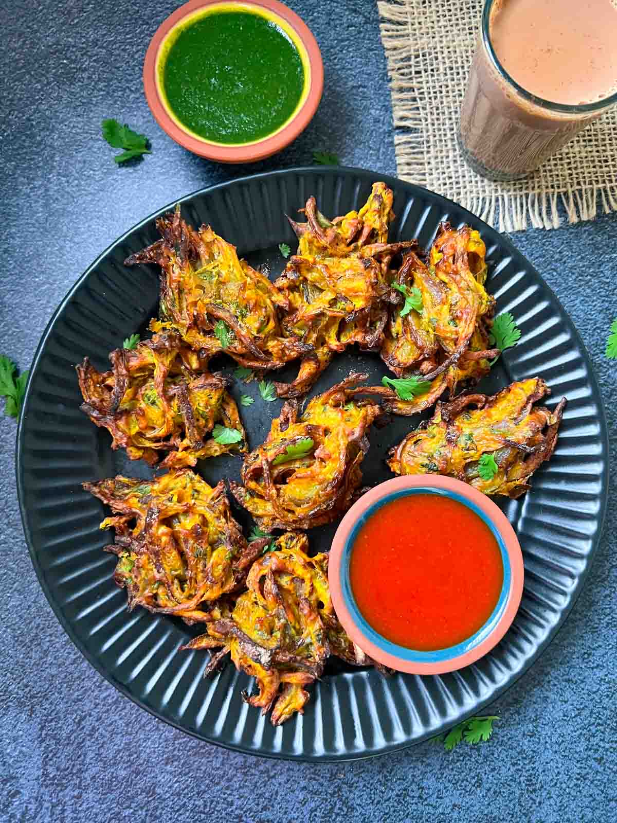 air fryer onion pakoda served on a plate with ketchup and green chutney on the side with tea