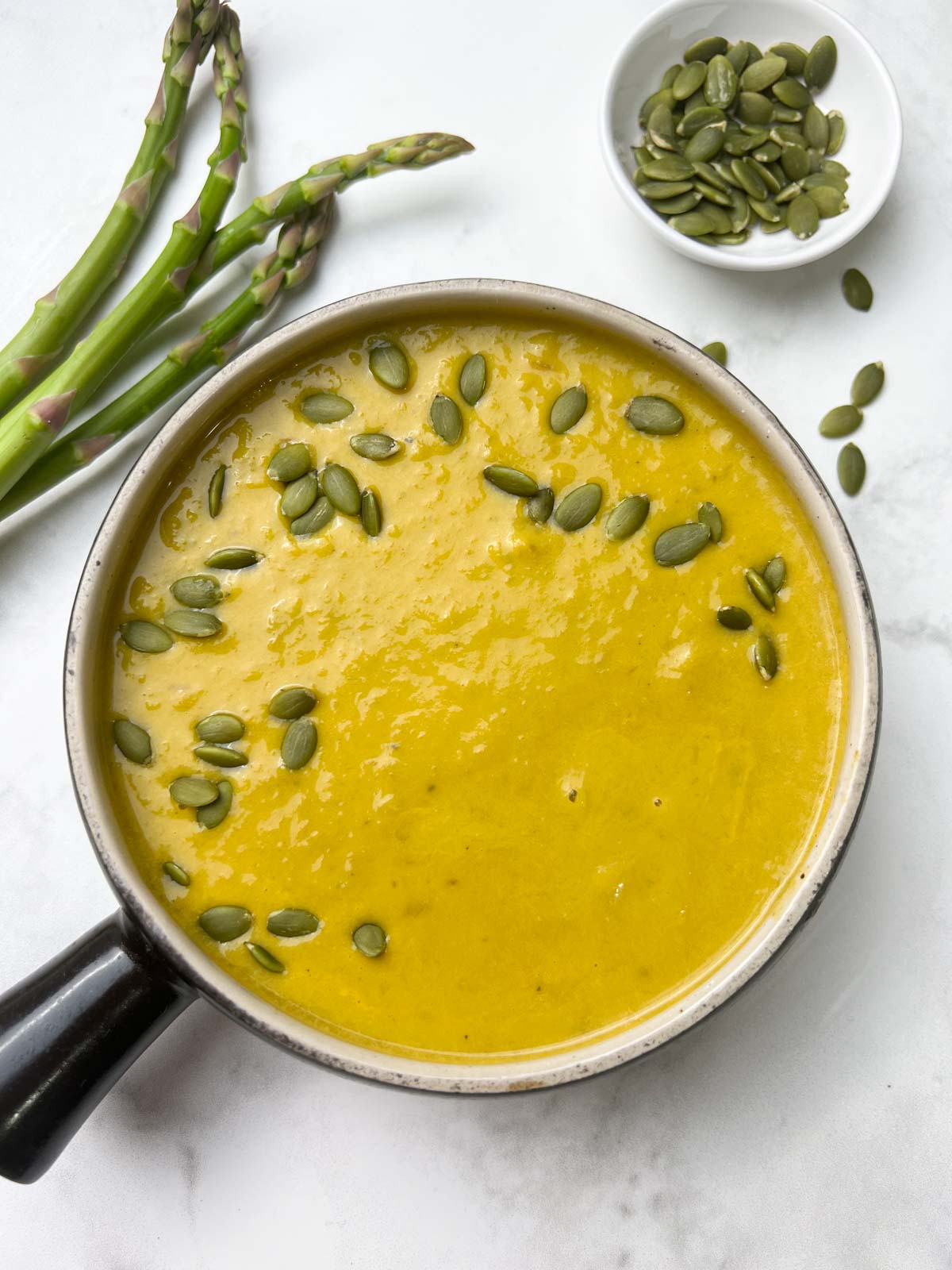 instant pot asparagus soup served in a soup bowl garnished with pumpkin seeds and asparagus and pumpkin seeds on the side 