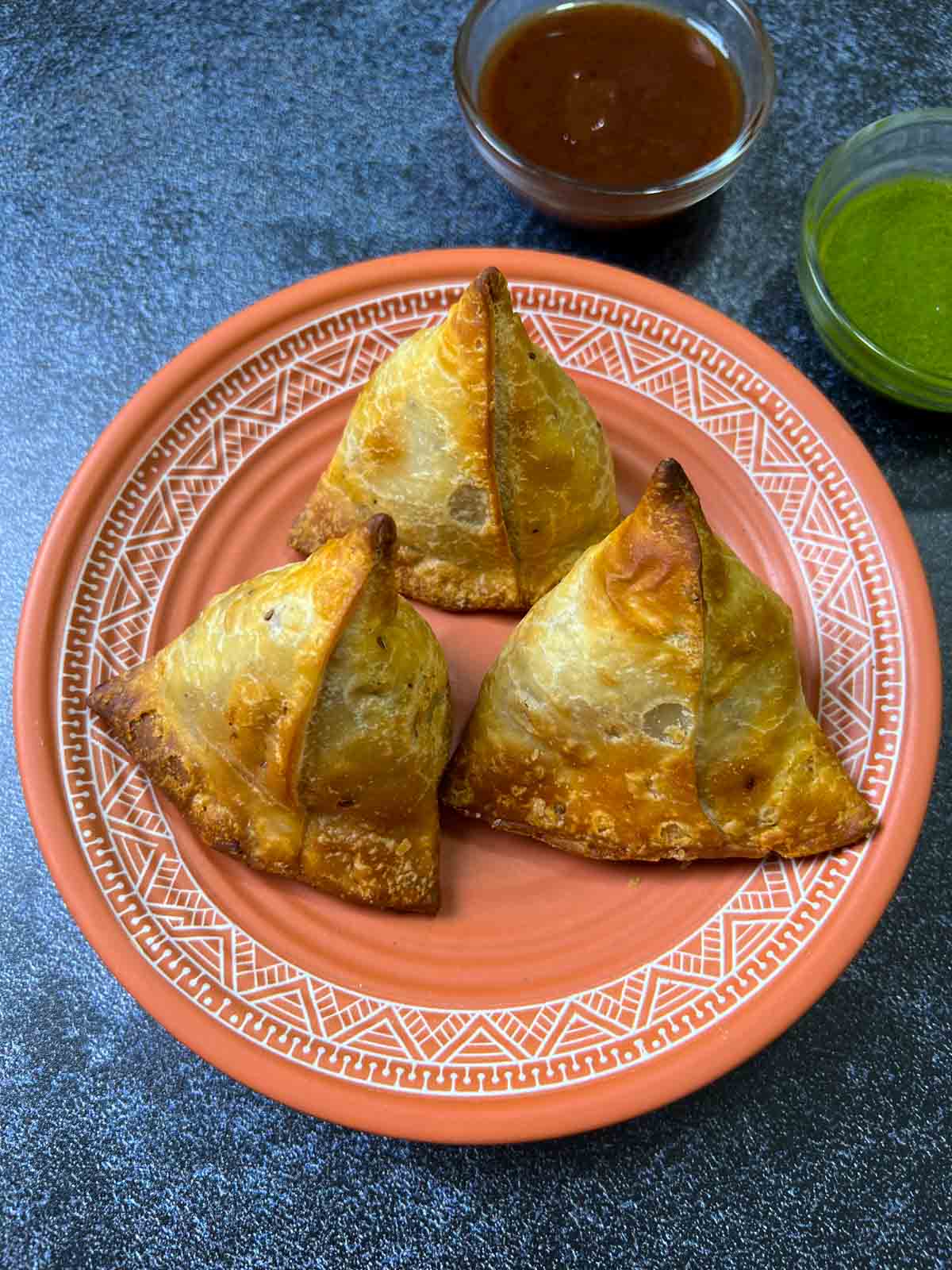air fryer samosas on a plate with chutneys on the side