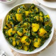 potato moringa leaves stir fry (aloo moringa) served in a white bowl with roti and salad on the side