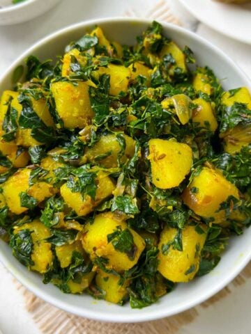 potato moringa leaves stir fry (aloo moringa) served in a white bowl with roti and salad on the side