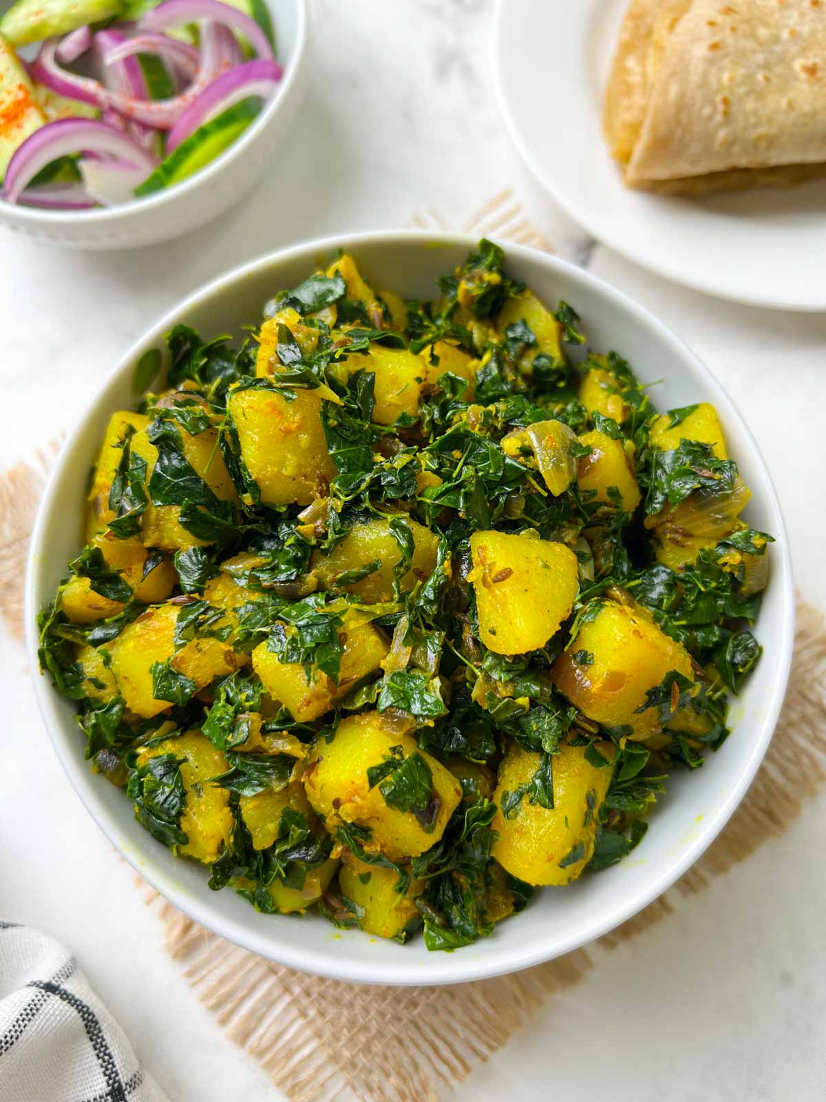 potato moringa leaves stir fry (aloo moringa) served in a white bowl with roti and salad on the side