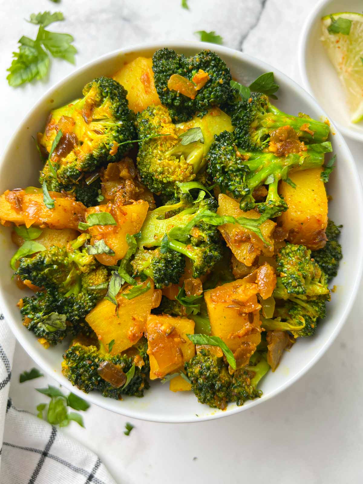 indian broccoli potato stir fry (aloo broccoli sabzi) served in a bowl with lime edge on the side
