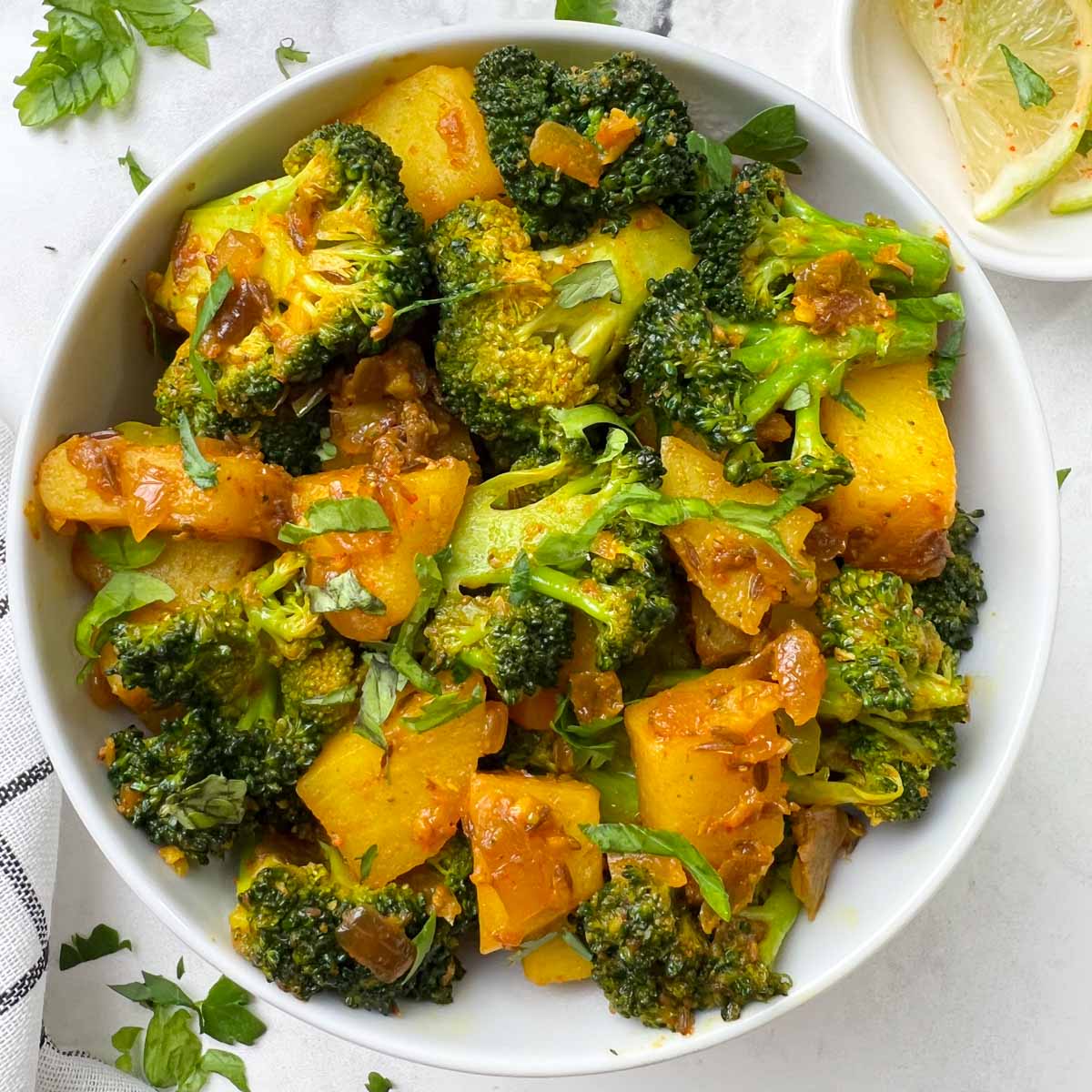 indian broccoli potato stir fry served in a bowl with lime edge on the side