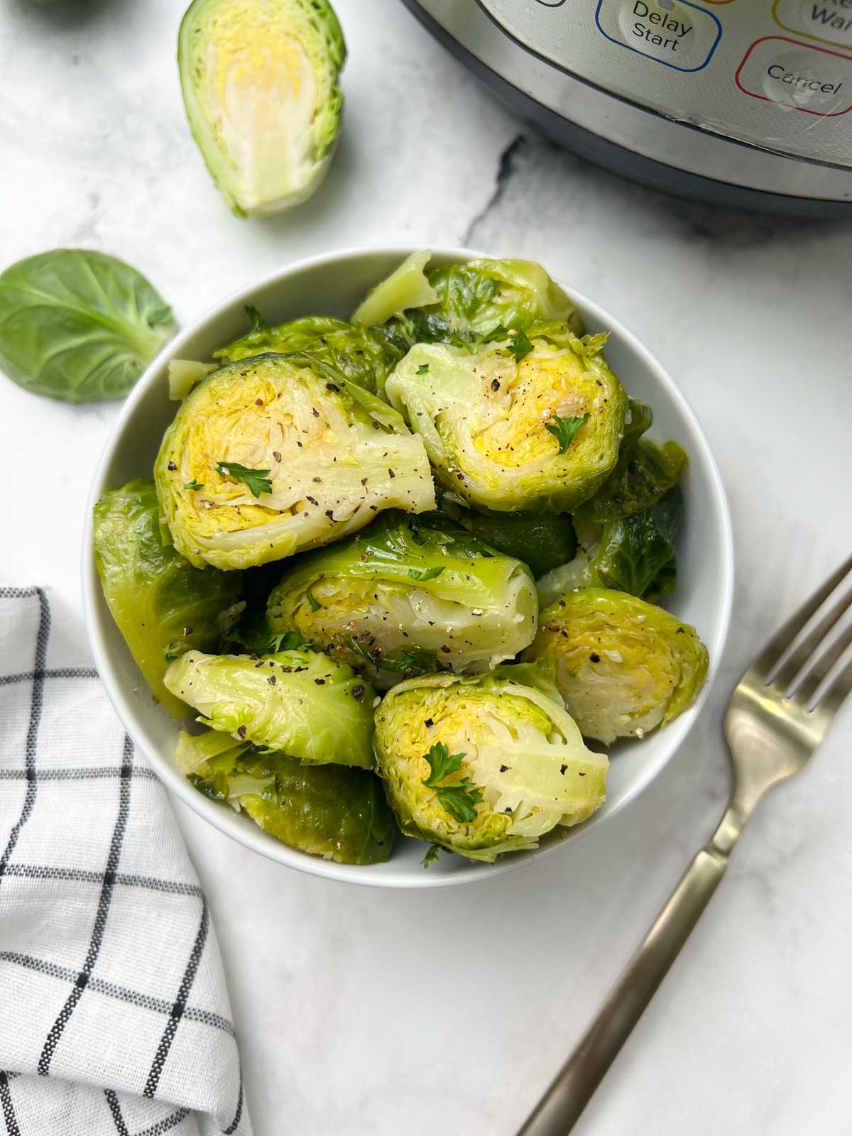 steamed and seasoned instant pot brussels sprouts served in a white bowl with fork on the side