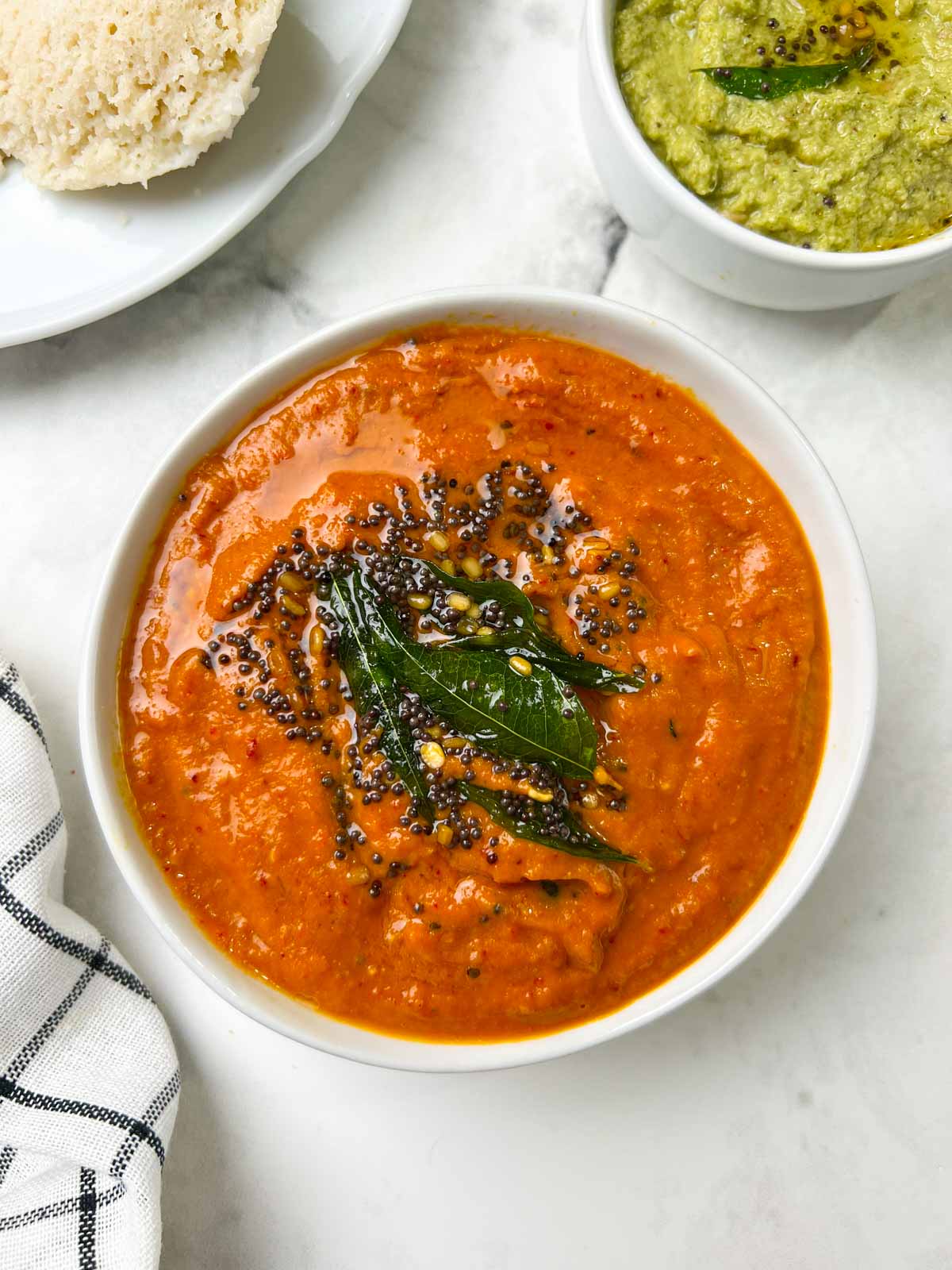 onion tomato chutney recipe served in a bowl with tempering on the top with side of coconut chutney and idli