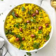 poha recipe served in a white bowl garnished with coriander leaves and roasted peanuts spoon on the side