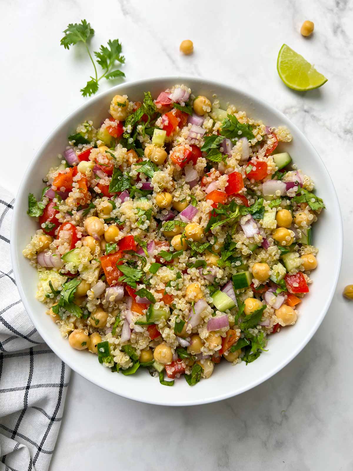 chickpea quinoa salad serve din a large white bowl garnished with herbs and lime wedge on the side