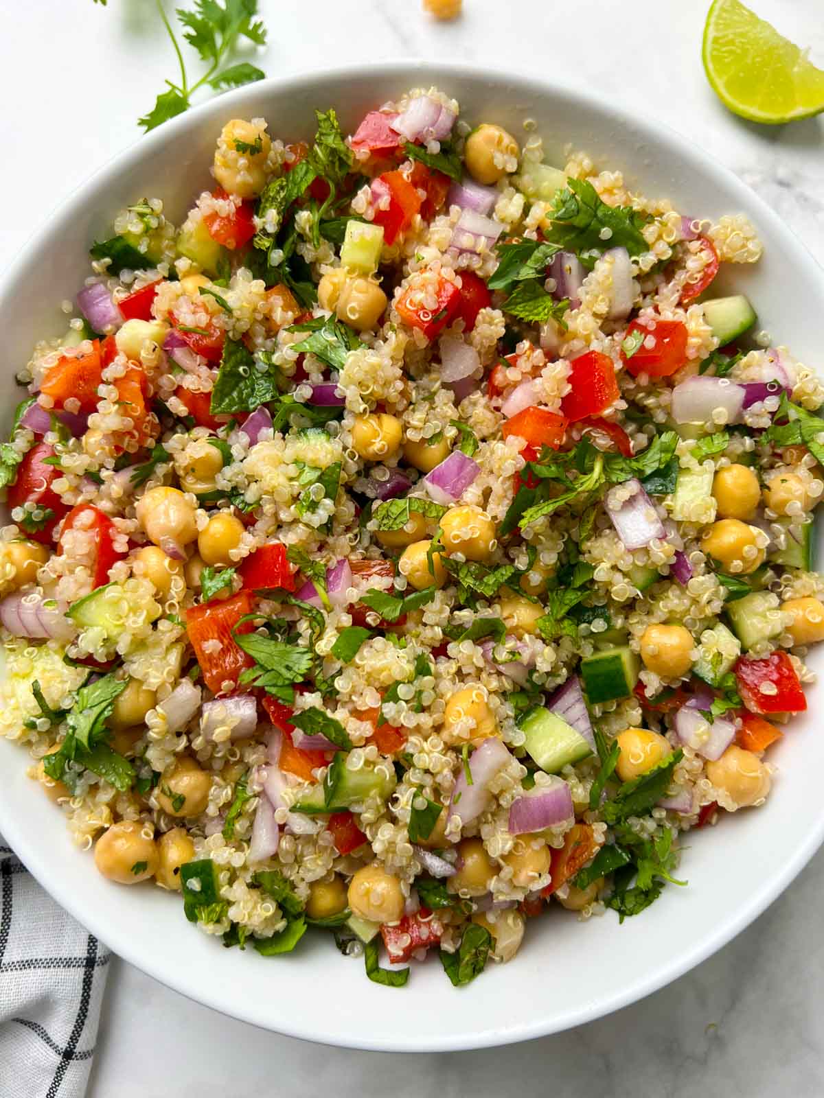 chickpea quinoa salad serve din a large white bowl garnished with herbs and lime wedge on the side