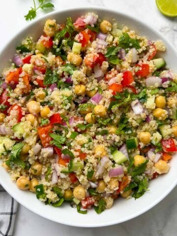 quinoa chickpea salad served in a white bowl garnished with cilantro and lime wedge on the side