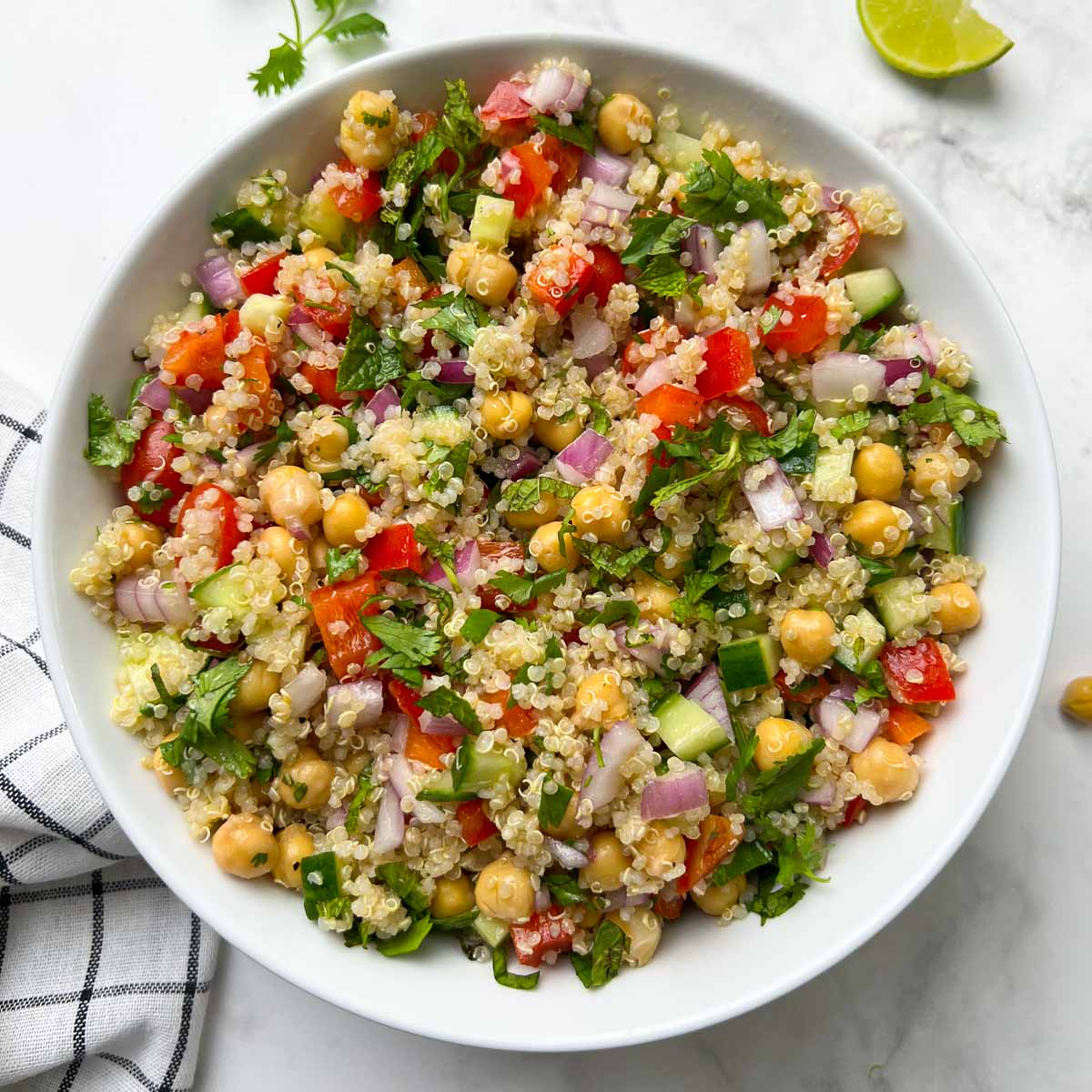 quinoa chickpea salad served in a white bowl garnished with cilantro and lime wedge on the side