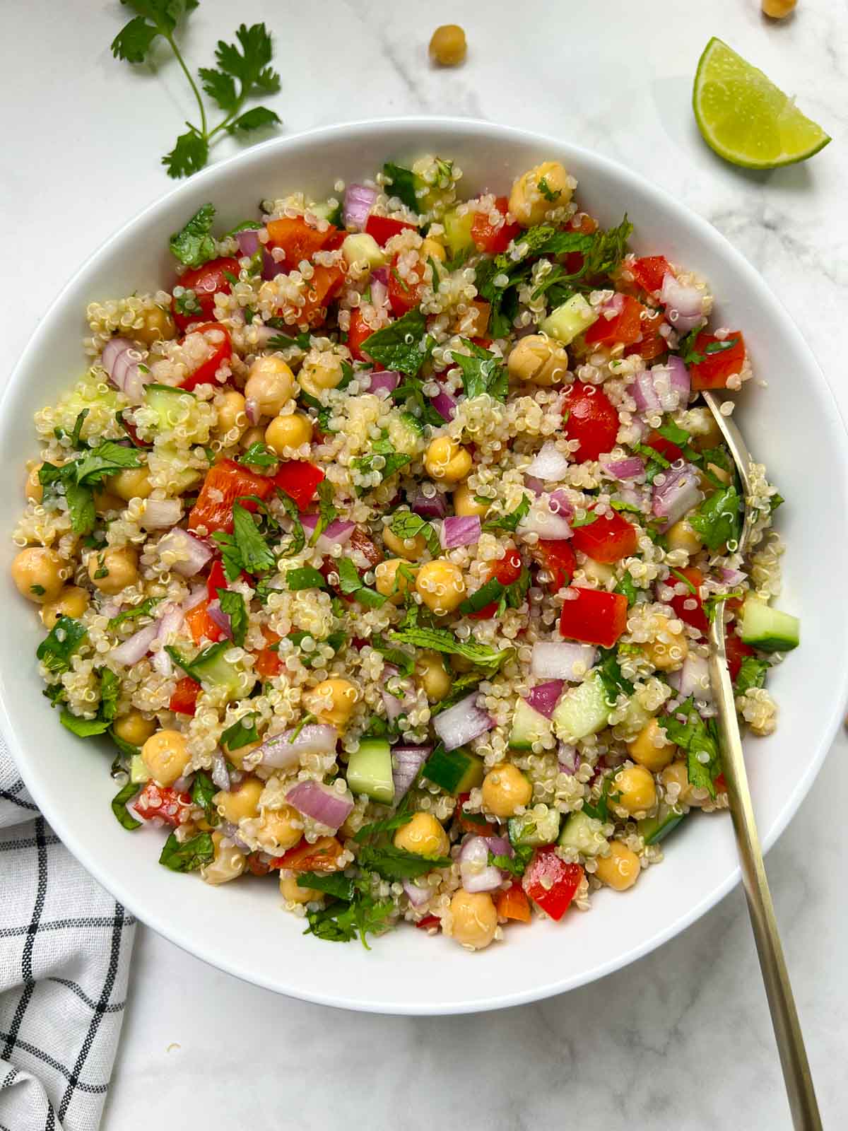 quinoa chickpea salad served in a white bowl garnished with cilantro with a spoon and lime wedge on the side