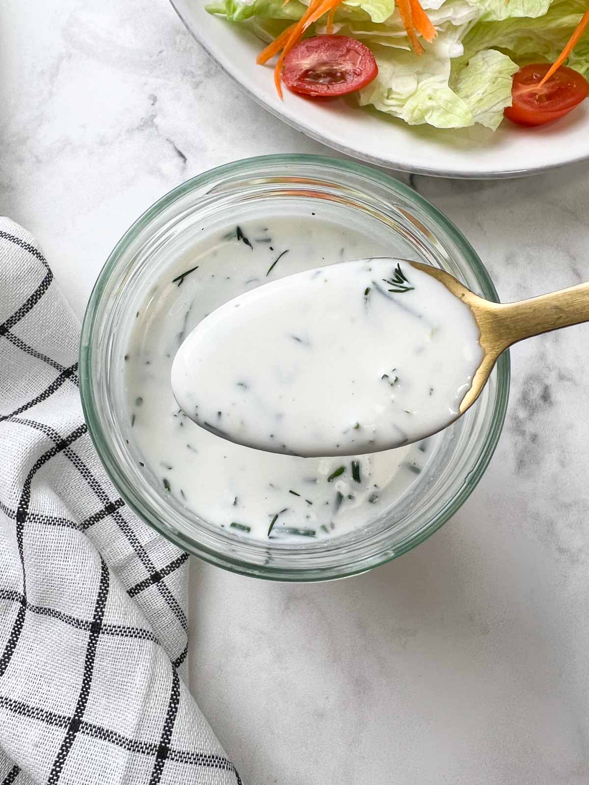 ranch dressing in a spoon with salad plate on the side