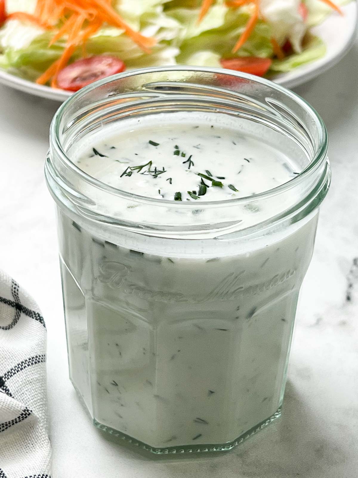 homemade ranch dressing in a mason jar with a salad plate on the side 