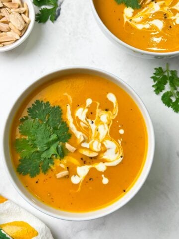 instant pot sweet potato soup served in two bowl garnished with coriander leaves, cream and slivered almonds and a cup of slivered almonds on the side