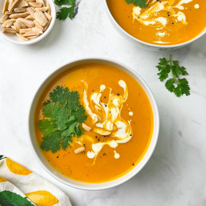instant pot sweet potato soup served in two bowl garnished with coriander leaves, cream and slivered almonds and a cup of slivered almonds on the side