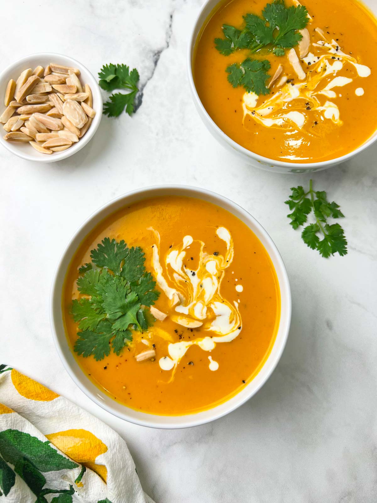 instant pot sweet potato soup served in two bowl garnished with coriander leaves, cream and slivered almonds and a cup of slivered almonds on the side