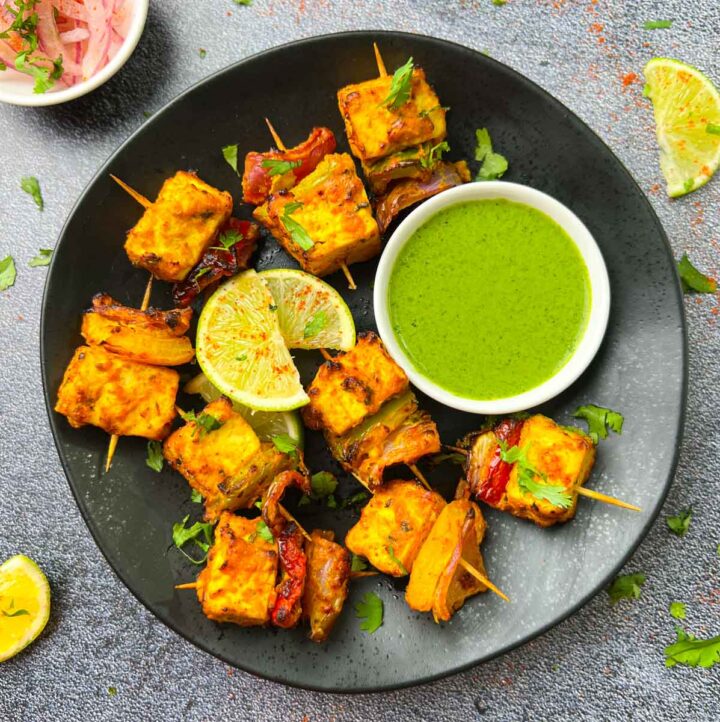 tandoori tofu tikka served in a plate with green chutney and onions, lime wedges on the side