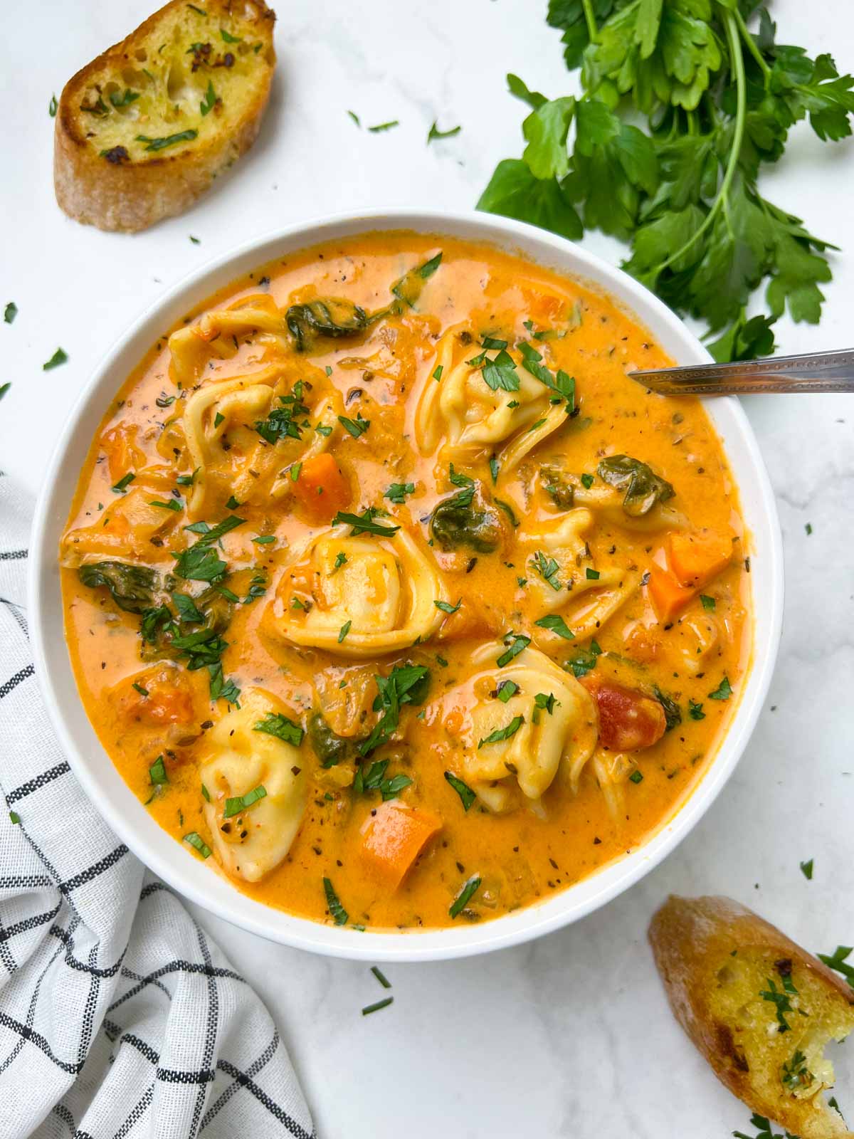 instant pot creamy tortellini soup served in a white bowl garnished with parsley with a spoon and garlic bread on the side