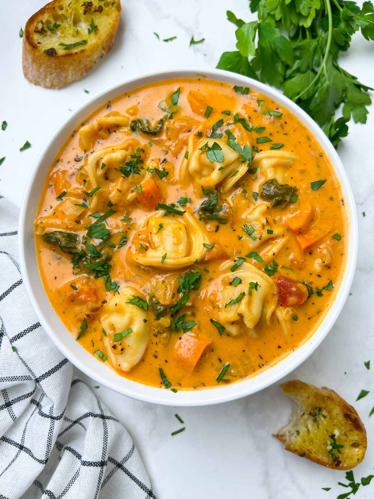 Instant Pot Creamy Tortellini Soup served in a white bowl garnished with parsley and garlic bread on the side