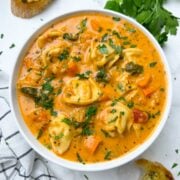 instant pot tortellini soup served in a bowl with garlic bread and parsley on the side.