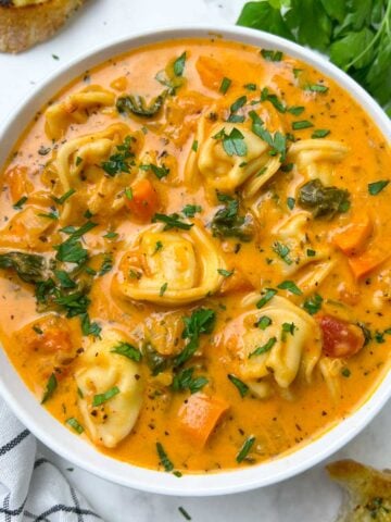 instant pot tortellini soup served in a bowl with garlic bread and parsley on the side.