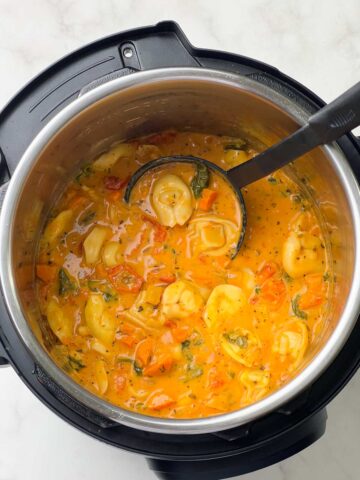 creamy tortellini soup in the instant pot insert with a ladle full of soup