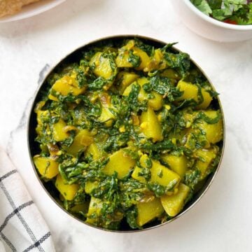 potato spinach stir fry served in a bowl with chapati and salad on the side