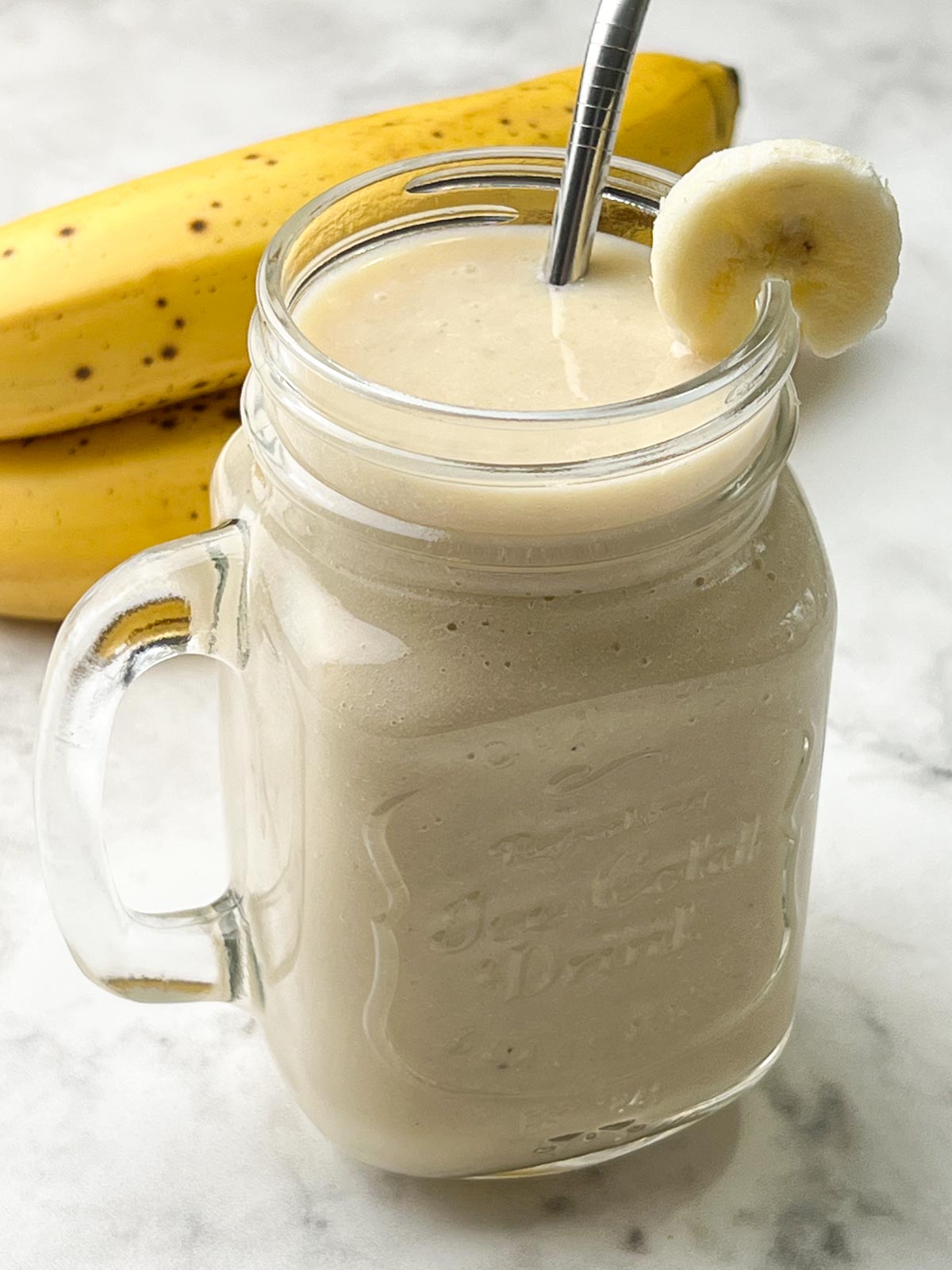 creamy banana juice recipe served in a mason jar garnished with banana slice and ripe banana on the side