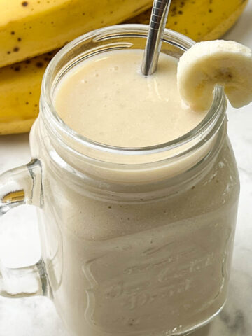 creamy banana juice recipe served in a mason jar garnished with banana slice and ripe banana on the side