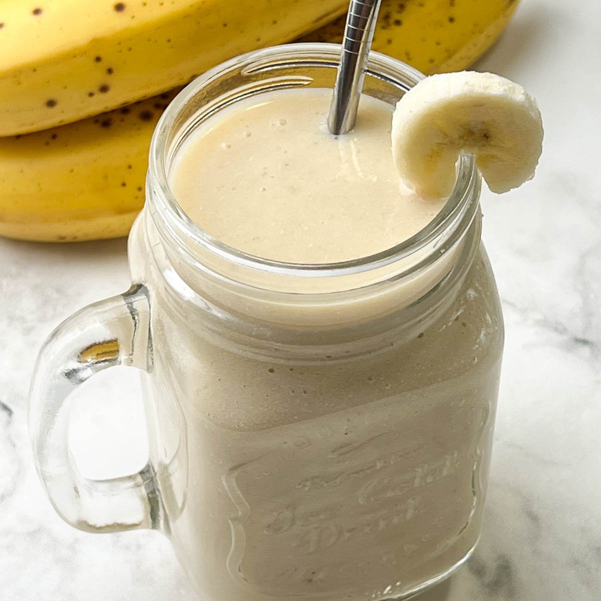 creamy banana juice recipe served in a mason jar garnished with banana slice and ripe banana on the side