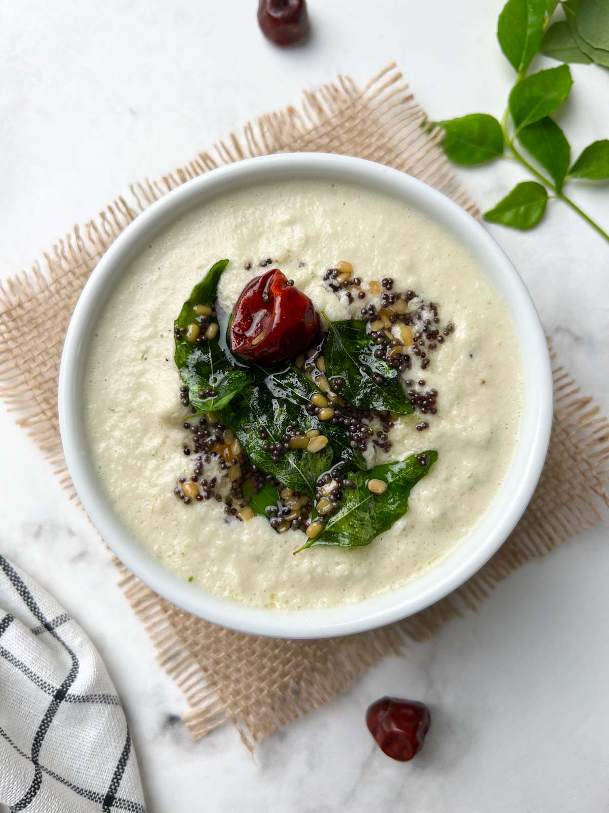 coconut chutney (nariyal chutney) recipe served in a white bowl with tempering on the top and curry leaves on the side