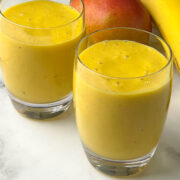 mango banana smoothie served in a serving glasses with whole mango and banana on the side