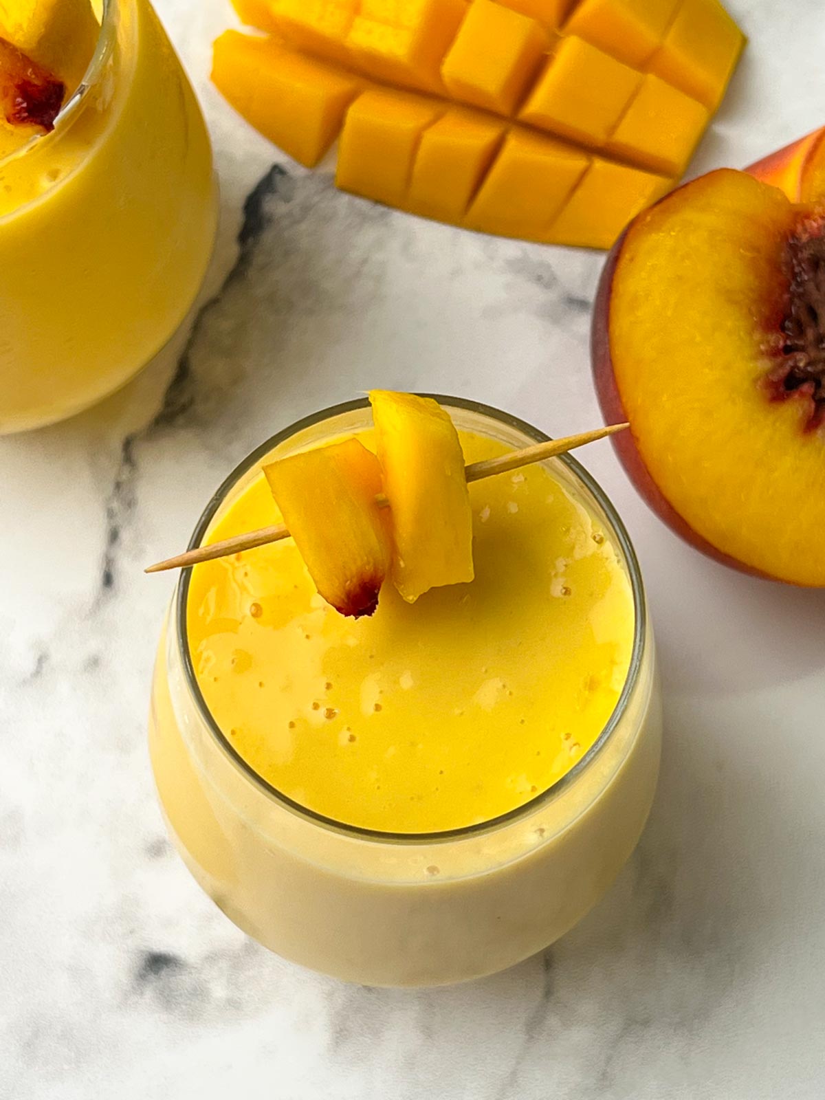 mango peach smoothie recipe served in a juice glass garnished with pieces of fruits in a toothpick