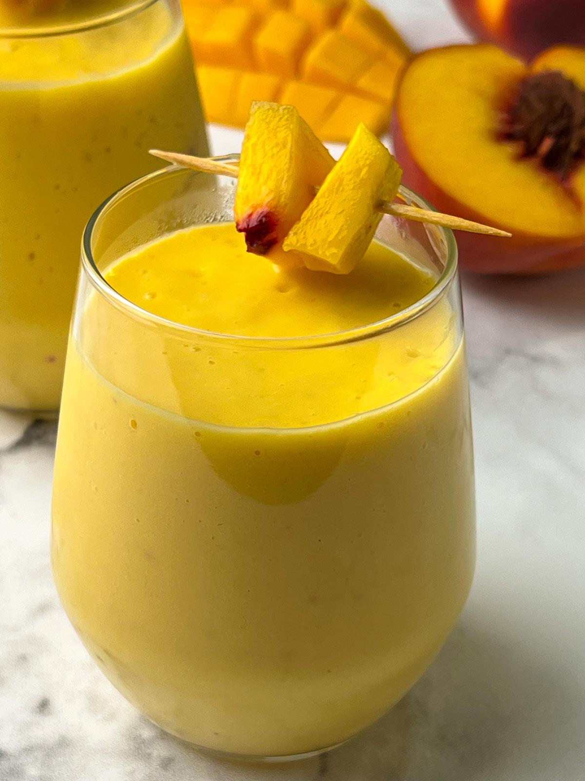 mango peach smoothie recipe served in a juice glass garnished with pieces of fruits in a toothpick