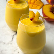 mango and peach smoothie served in a glass garnished with pieces of fruits in a toothpick