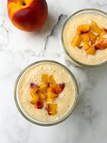 peach banana smoothie served in juice serving glasses topped with chopped yellow peach pieces