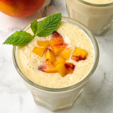 peach banana smoothie served in juice serving glasses topped with chopped yellow peach pieces with mint leaf garnished