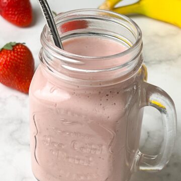 strawberry banana milkshake served in a mason jar with a steel straw with fruits on the side