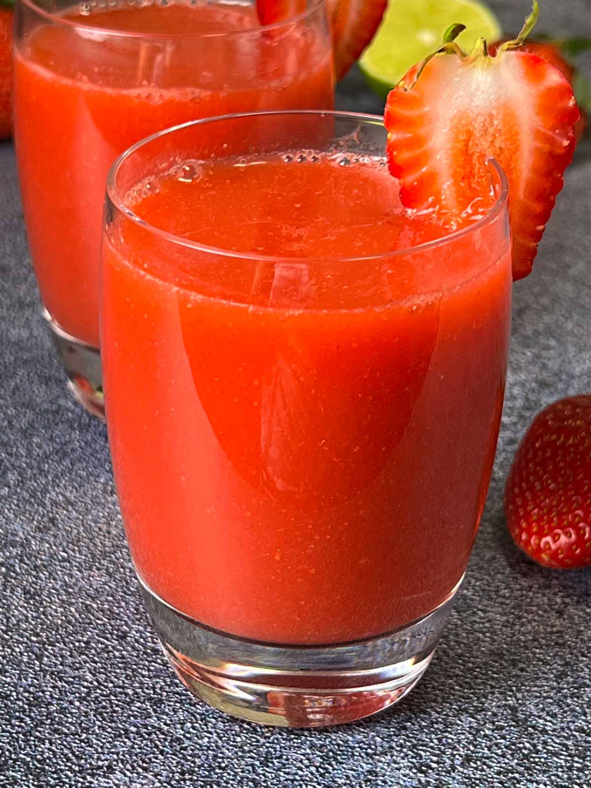 fresh homemade strawberry juice served in two serving glasses garnished with sliced strawberries on top