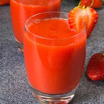 fresh homemade strawberry juice served in two serving glasses garnished with sliced strawberries on top