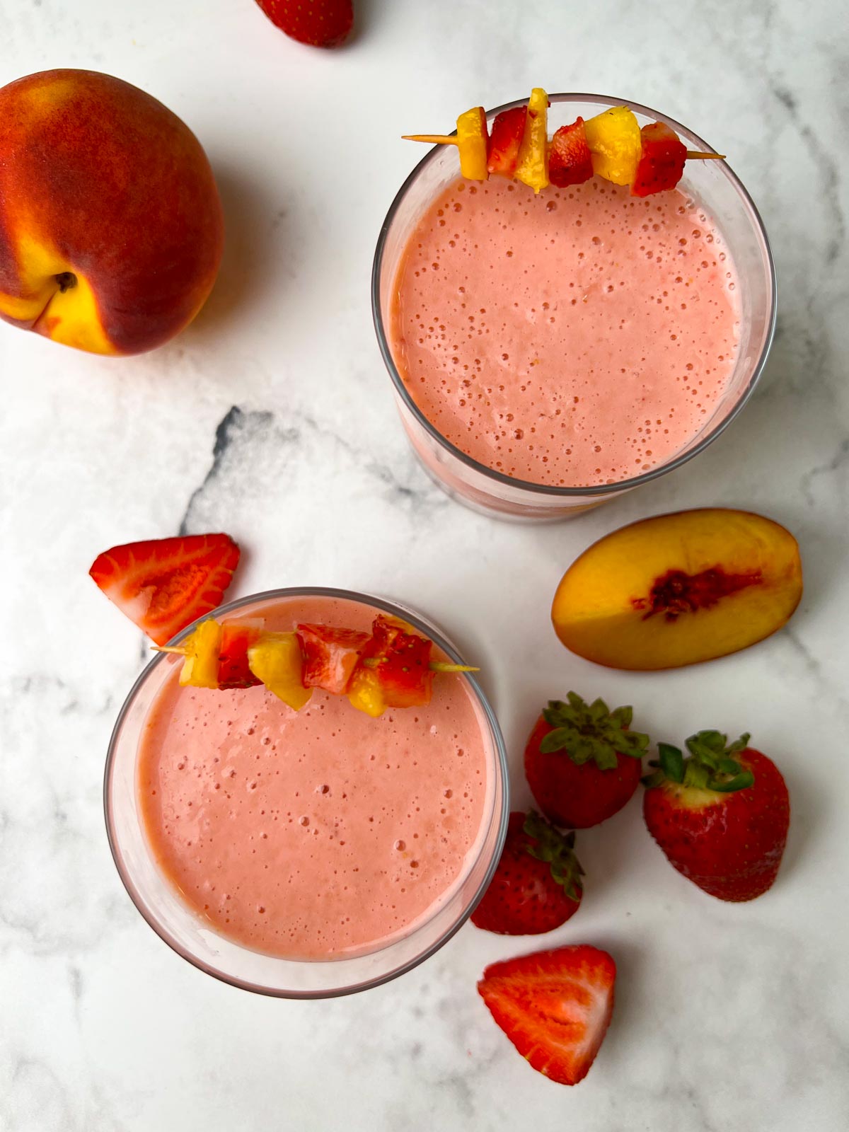 strawberry peach smoothies in juice glasses garnished with peach and strawberry skewers with fruits on the side