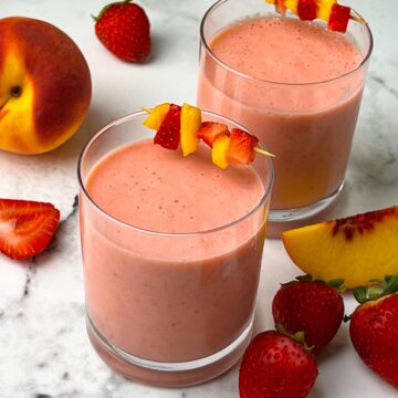 strawberry peach smoothie in juice glasses garnished with peach and strawberry skewers with fruits on the side