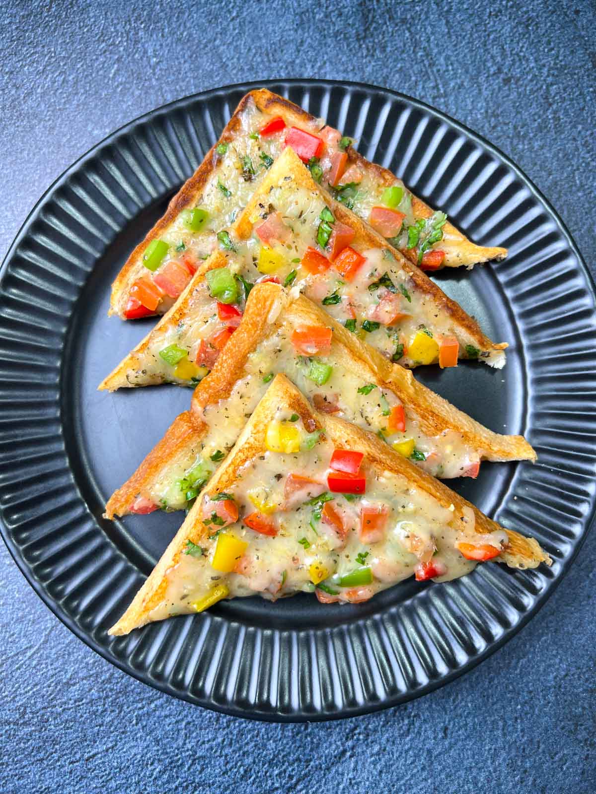 Veg chili cheese toast placed in a layer on a black plate