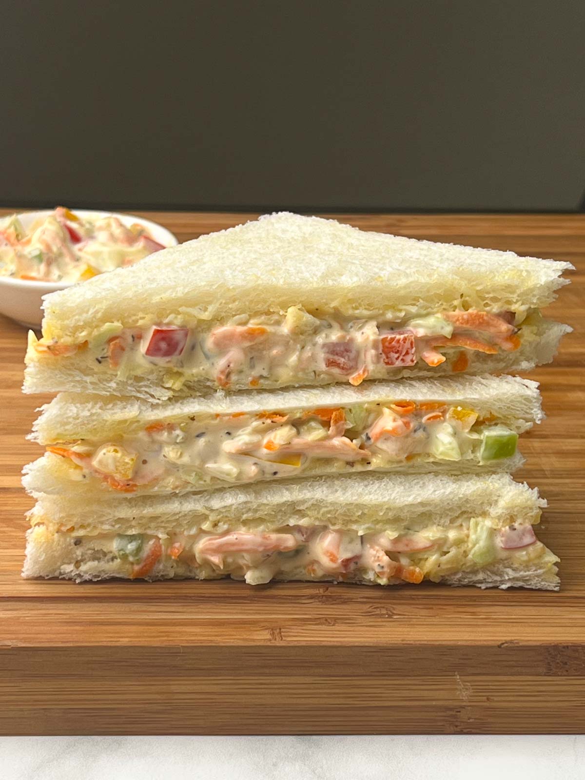 vegetable mayonnaise sandwich stacked on one another on a wooden board