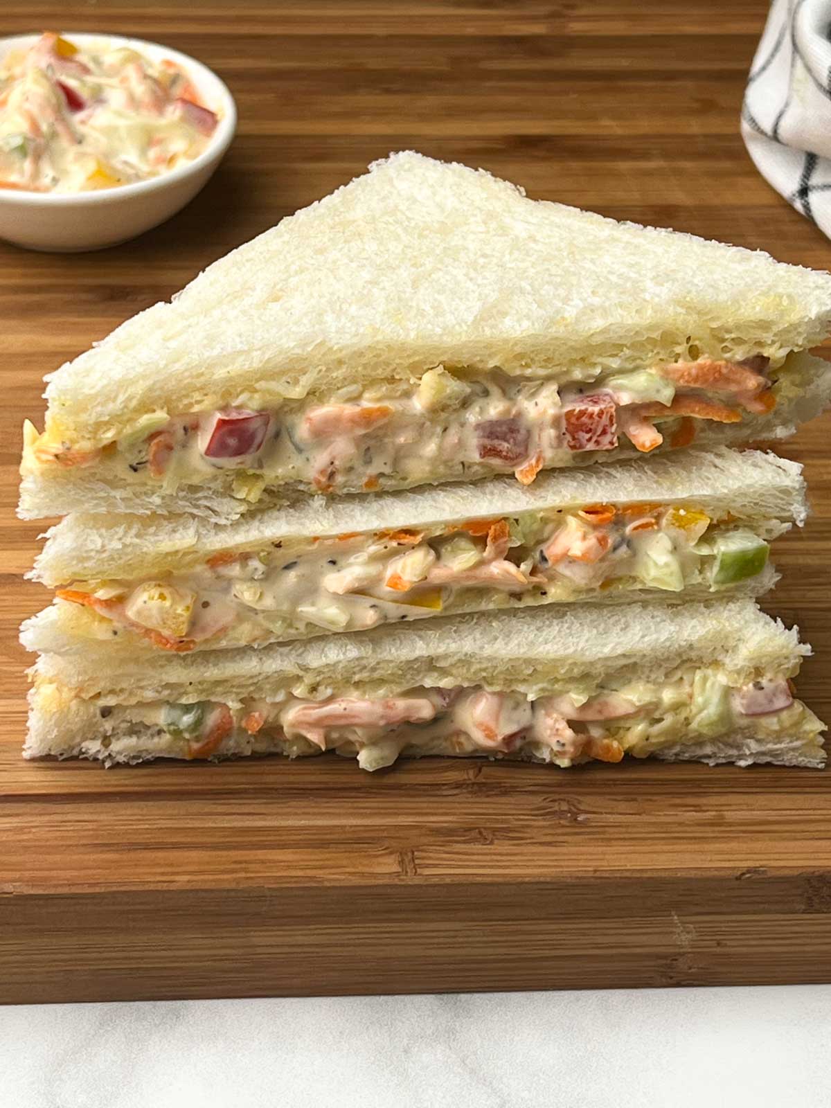 veg mayo sandwich stacked on a wooden board with vegetable-mayonnaise mixture on the side